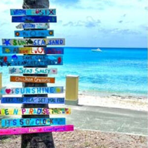 A colorful, rustic sign on a beach in St. Croix with phrases like "Sunshine" and "Sun Sea Sand".