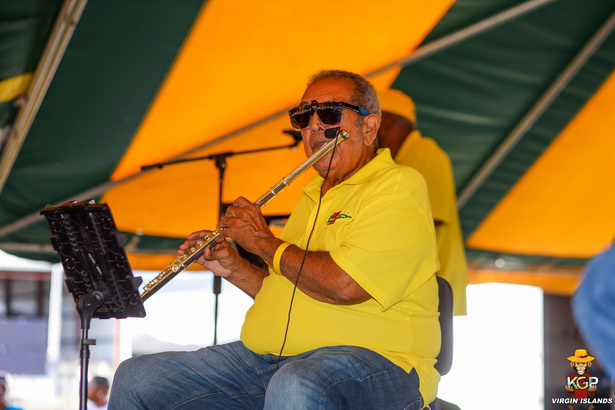 A man playing a flute under a yellow tent at the Agricultural Fair.